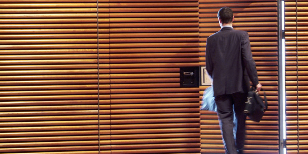 A businessman is seen from behind as he exits the door of a wood-paneled office. A businessman is seen from behind as he exits the door of a wood-paneled office.