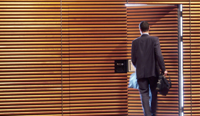 A businessman is seen from behind as he exits the door of a wood-paneled office.  A businessman is seen from behind as he exits the door of a wood-paneled office.