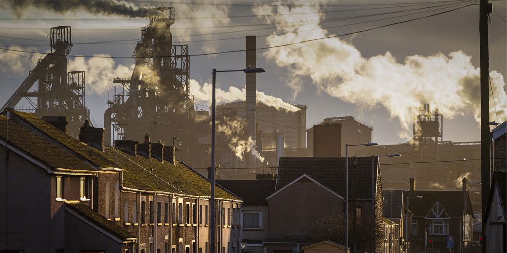 A factory with billowing smokestacks looms behind the houses of a small town. A factory with billowing smokestacks looms behind the houses of a small town.