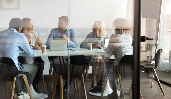 Five colleagues meet and collaborate around a table in a glass-walled conference room Five colleagues meet and collaborate around a table in a glass-walled conference room