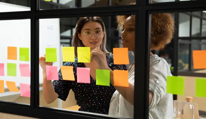 Two coworkers have a discussion at a glass whiteboard Two coworkers have a discussion at a glass whiteboard