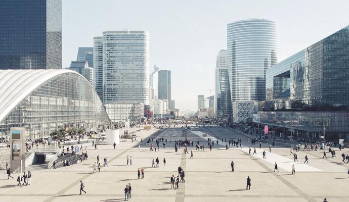 People move through a large, open outdoor plaza that is bounded by modern office buildings