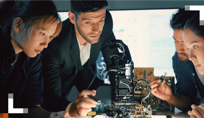 A team of young professionals gathers around a robotics model to work on it together