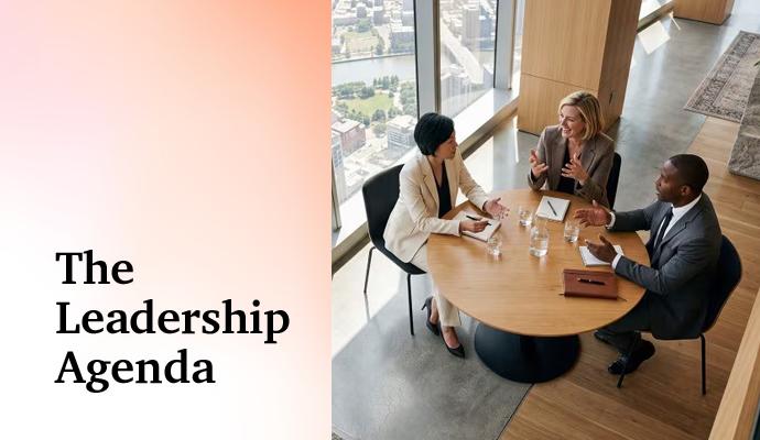 Three professionals engage in conversation at a round table in a modern office with a city view behind them. Three professionals engage in conversation at a round table in a modern office with a city view behind them.